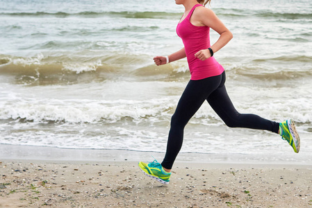 运动女子跑在海洋海滩复制空间。 女跑步者在夏季晨边观看。 无法辨认的身体慢跑。 健康生活方式概念