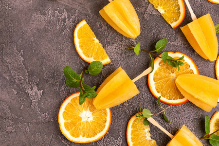 自制橙色冰棒，成熟橙色和新鲜薄荷在灰色混凝土背景。 健康的甜点。 无乳糖冰淇淋。