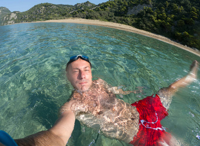 游泳的家伙在海里自拍。 背景中的偏远岛屿