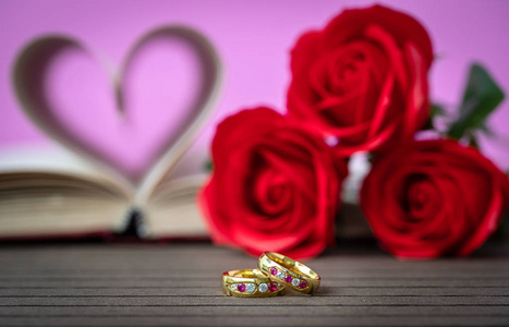 书页弯曲成心形，有红色玫瑰和结婚戒指。 爱的概念，心形从书页