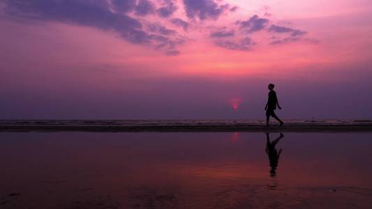 剪影。孤独的亚洲年轻人在日落时平静地沿着荒芜的海滩散步。海景