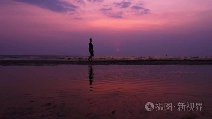 剪影. 夕阳下,孤独的亚洲年轻人平静地沿着一片荒芜的海滩散步. 海景.