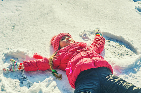 一个快乐的孩子正在外面的冬天玩耍。 那个女孩做了个雪天使。