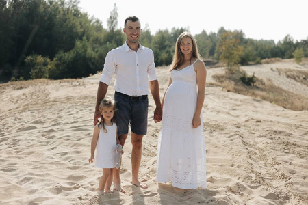 白种人家庭的肖像与婴儿在白色的衣服站在沙滩上。怀孕的普普。新生儿