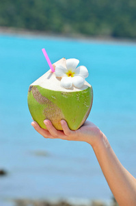女人手中的椰子鸡尾酒在绿松石的大海上