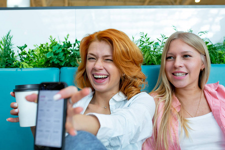 在商场的咖啡馆里, 两个快乐的女性朋友用手机