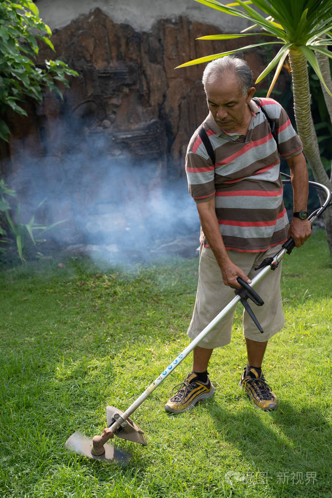 高级亚洲人在自己的家花园割草