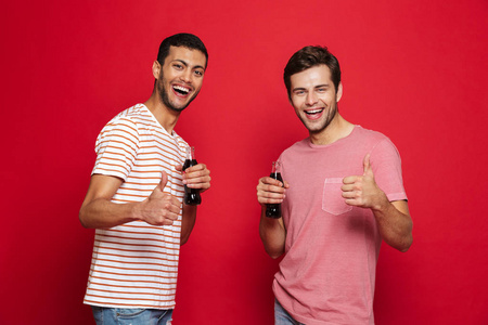 两个快乐的年轻人站在红色背景下，从瓶子里喝苏打水