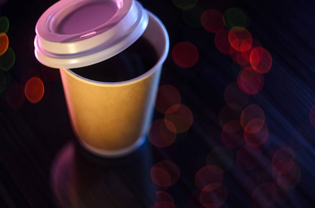 桌上一杯外卖咖啡..背景上的波克灯。模型的概念，背景。纸杯塑料盖模糊背景圣诞薄膜