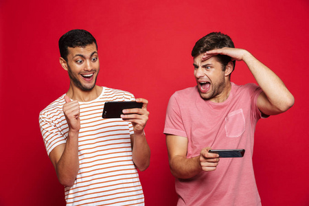 两个兴奋的男性朋友站在红色背景下玩手机游戏