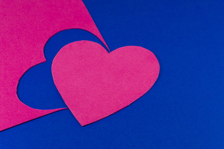 心切出明亮的粉红色泡沫片，在完整的框架背景下观看。 从上面看到蓝色床单上明亮的粉红色心脏。 爱情与关系情人节与色彩趋势概念