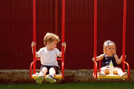 金发在秋千上的小孩子. 女孩和男孩的发型. 弟弟和妹妹喜欢一起玩.