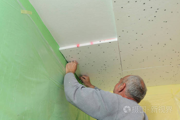 工人将发泡胶保温贴在室内工程的天花板上