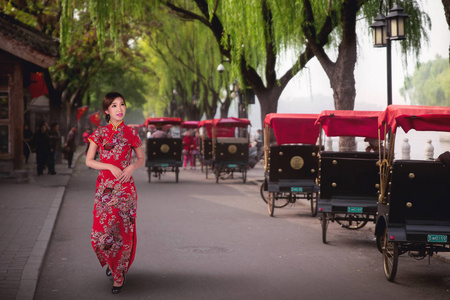 黄包车中国女士穿着红色旗袍,在北京的老中国胡同里骑着北京传统的