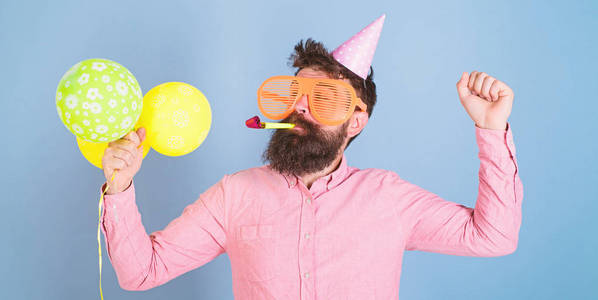 大胡子男子在生日帽和巨大的疯狂眼镜跳舞, 党硬, 有趣的时间概念。时髦与修剪胡子和胡子摆在党口哨和明亮的气球在蓝色背景下