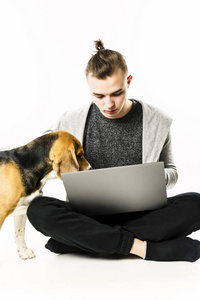 男人和狗猎犬一起在白色背景下看着地板上的笔记本电脑