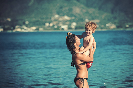 暑假和到海洋旅行。母亲带着儿子在水里游泳。加勒比海的幸福家庭。马尔代夫或迈阿密海滩活动的喜悦。小男孩在女父母手中的母亲节