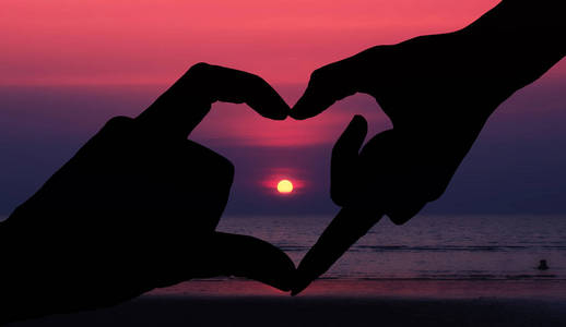 两只手的剪影，在傍晚美丽的夕阳天空中制作心脏符号。