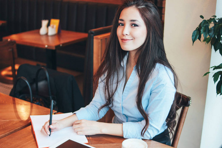 美丽迷人的黑发微笑的亚洲女孩在咖啡馆学生自由职业者的餐桌上工作或学习