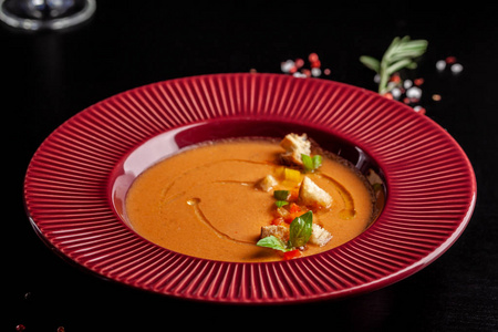 西班牙美食的概念。 新鲜西红柿的番茄汤加西番茄。 在餐馆的黑桌上，红色盘子里有漂亮的菜肴。 背景图像。 复制空间