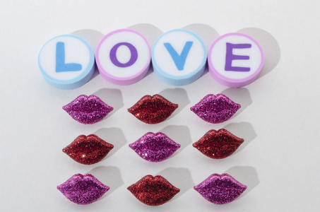 爱这个词是由圆形橡皮和小红紫色嘴唇在白色背景下制成的。 情人节装饰