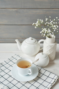 茶壶旁边的茶杯里的绿茶和一个木制背景上有婴儿气息的花瓶