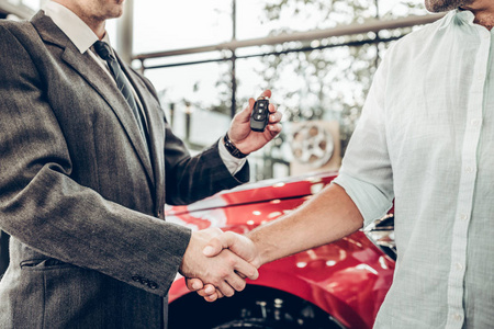 汽车商务汽车销售交易手势和人的概念密切关注经销商给新车主钥匙和握手在车展或沙龙