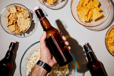 有选择的焦点男人拿着瓶子，啤酒在白色背景的碗里的零食附近