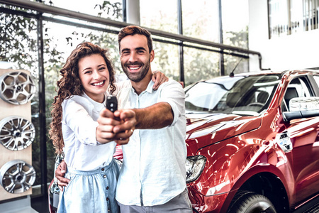 第一次大买一起。 一对幸福的年轻夫妇在汽车沙龙拥抱的肖像，展示了一辆新买的车的车钥匙。