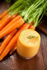 玻璃中的胡萝卜汁和木制背景上的新鲜胡萝卜。 健康食品概念