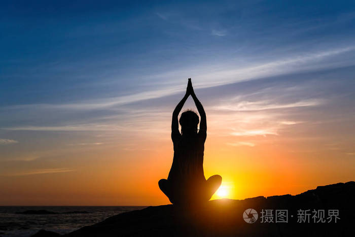 剪影年轻的冥想女人在日落时在海滩上练习瑜伽