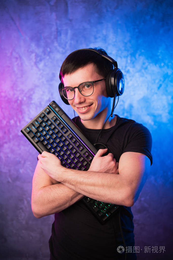 职业男孩玩家拿着游戏键盘在五颜六色的粉红色和蓝色霓虹灯的墙壁游戏