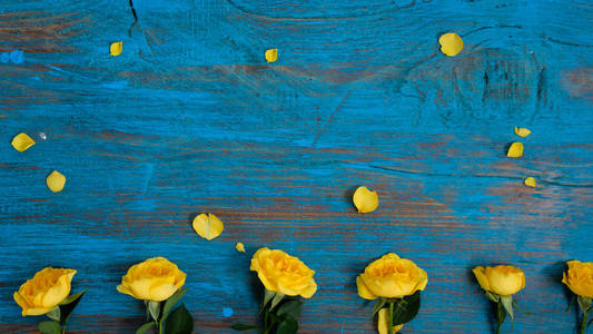 花的组成。 蓝色木制背景上由黄色花朵制成的框架。 复活节春季夏季概念。 平躺顶部vi