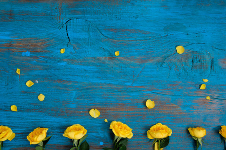 花的组成。 蓝色木制背景上由黄色花朵制成的框架。 复活节春季夏季概念。 平躺顶部vi