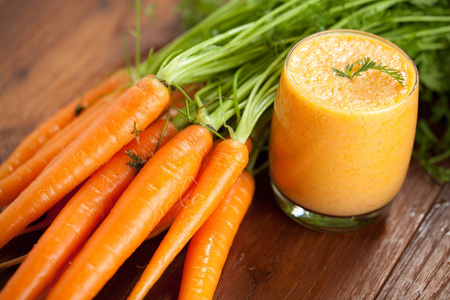 玻璃中的胡萝卜汁和木制背景上的新鲜胡萝卜。 健康食品概念