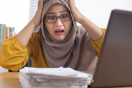 亚洲穆斯林女商人的肖像，疲惫，病态，压力，震惊，头痛的姿态，因为更多的纸张工作，在办公室工作过度