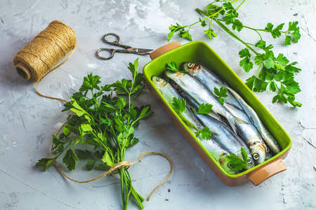 沙丁鱼或波罗的海青鱼在绿色盘子上，欧芹在浅灰色混凝土台面上。 生的未煮熟的海鱼。