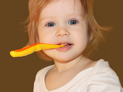 一个小女孩学会刷牙。 矮眼睛的女婴拿着她的牙刷，牙齿看起来笔直，对她的恶作剧微笑。