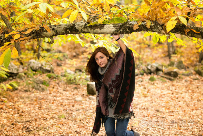 在秋天的森林里, 一个头发发红的年轻女子从树枝下经过