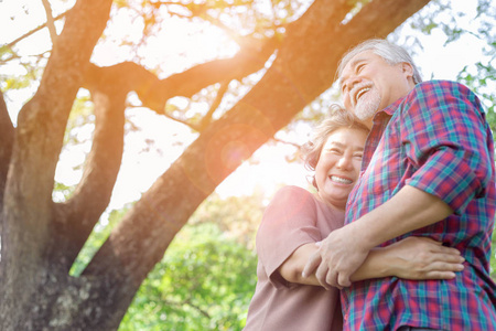 描绘幸福的老夫妇。迷人的祖父和祖母在公园里用爱和笑脸拥抱对方。祖父母身体健康，享受阳光下的生活