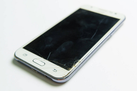 白色手机躺在白色的背景上。 手机屏幕坏了。 损坏的玻璃表面。 智能手机设计。 小玩意。
