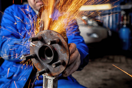 汽车修理工在汽车修理车间用金属磨床切割汽车零件,背景工具中明亮的