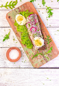 三明治与鲱鱼片与新鲜的绿色沙拉，洋葱圈，一半的鸡蛋和微绿色在木桌上。