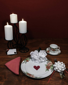 花型精美瓷器餐具，配配盘子杯和碟子。 白色玫瑰花束，粉红色餐巾，银器，白色蜡烛和卡片