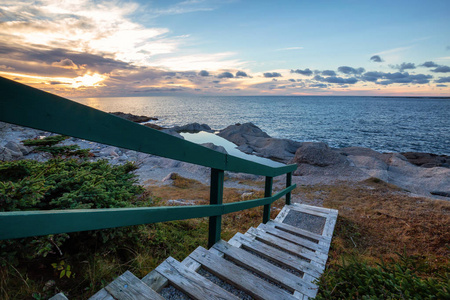 在一个充满活力的日落中，木楼梯下到一个美丽的岩石大西洋海岸。 拿在牛头纽芬兰加拿大。