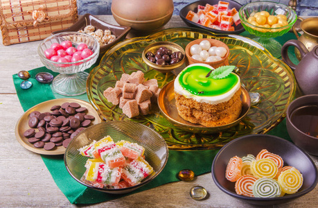 茶休息与美味的蜂蜜蛋糕装饰形式的绿色苹果和各种颜色的小糖果。 铜和粘土板的组成与水壶。 阿拉伯概念。