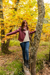 在秋天的森林里, 一个年轻的女孩在地上掉落的树干上留着红色的头发平衡