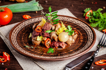 法国菜的概念。 小牛肉和蘑菇，全炖洋葱，胡萝卜和辣椒。 在餐馆里在蔬菜旁边的陶瓷盘子里端菜。