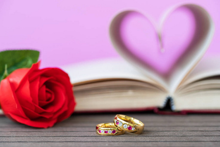 书页弯曲成心形，有红色玫瑰和结婚戒指。 爱的概念，心形从书页