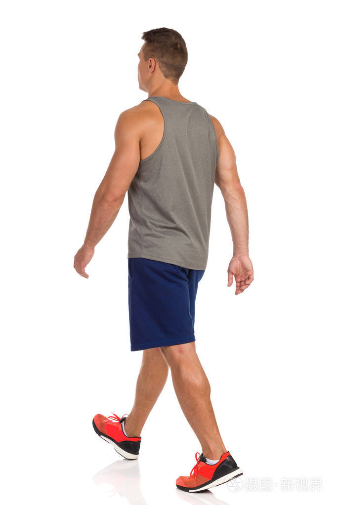 穿着蓝色短裤,灰色坦克上衣和橙色运动鞋的年轻人正在走路. 后侧视图.